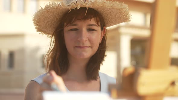 Portrait of Happy Inspired Female Painter in Straw Hat Smiling Making Paint Strokes in Slow Motion alt