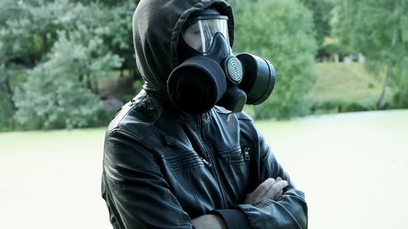 Man in Gas Mask Leather Jacket with Hood Standing Outdoors at Forest Near Lake