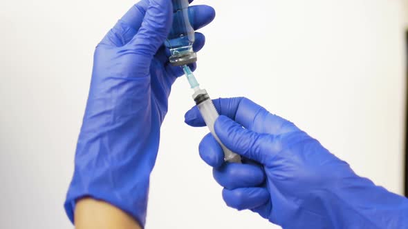 Health Worker Dials the Vaccine From Ampoule Into a Syringe Wearing Blue Protective Gloves alt
