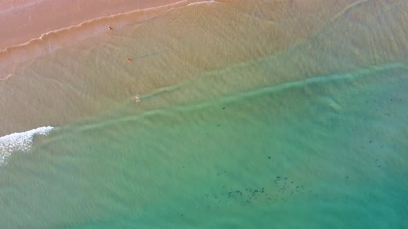 Scenic drone aerial view of the beach and ocean with calm waves during a sunset with vibrant colors.