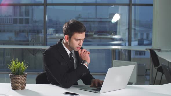 Portrait of Young Attractive Businessman Working at Laptop in Office.