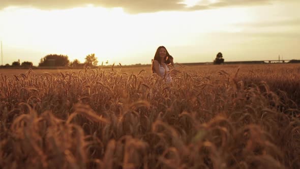 Beautiful Young Woman Enjoys Life Walking on a Wheat Field at Sunset