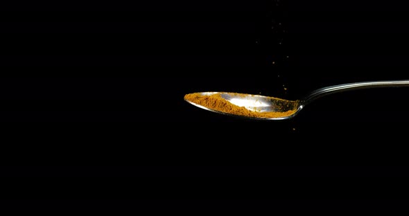 Spoon and Curry Powder falling against Black Background, Slow motion 4K alt