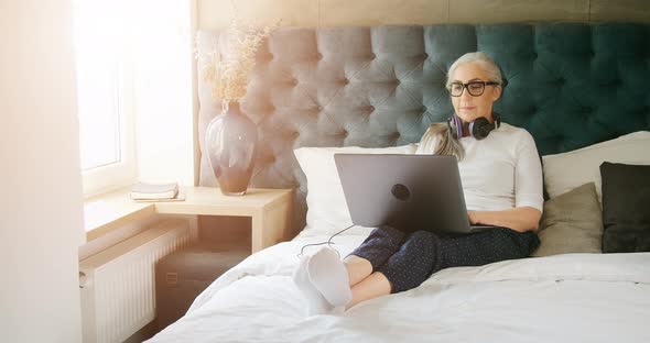 Elderly Woman with Laptop in Bedroom