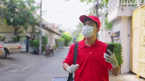 Asian delivery man in red uniform with face mask carrying bag of food delivering food to customer alt