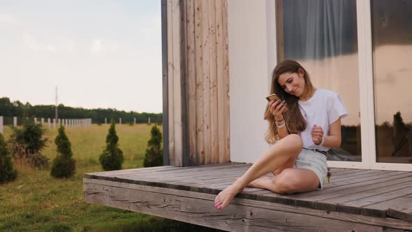 Portrait of Young Beautiful Woman Using Mobile Phone at House Porch