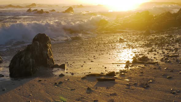 Small waves crashing onto beach during golden sunset in background. alt