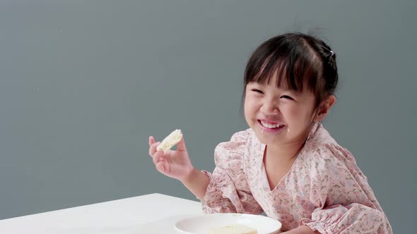 Happy little Asian girl rubs her eyes, smile, and enjoy eating crispy butter toast at home. alt
