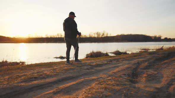 Side View a Man Sport Fitness Nordic Walking with Special Stick on the Ground Next to Water alt