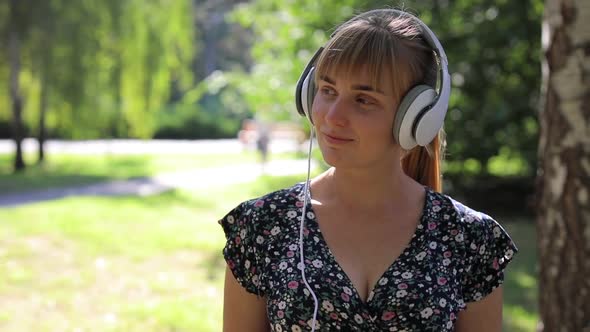 Woman Walking in the Park in Headphones and Listening Music