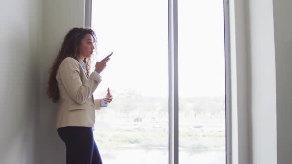 Biracial businesswoman smiling and talking on smartphone in modern interiors alt