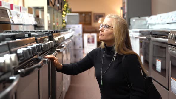 Pretty mature blonde woman looking at the features and benefits of a gas stove in a kitchen applianc alt