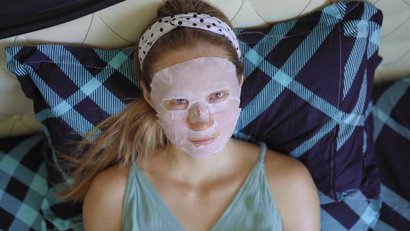 A Young Woman Laying on a Bed with a Cosmetical Face Mask on Her Face. Skincare Concept alt
