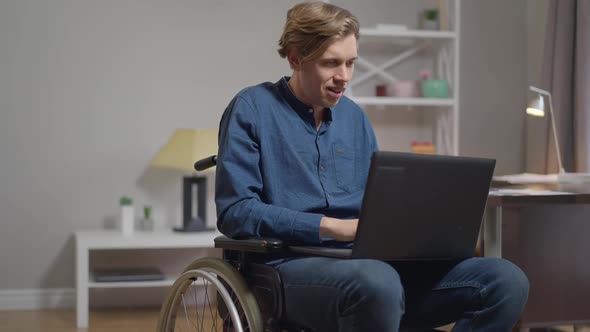 Portrait of Confident Absorbed Young Disabled Man Texting on Laptop Keyboard Looking at Camera alt