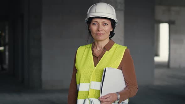 Portrait of female caucasian engineer holding document while standing on construction site. alt