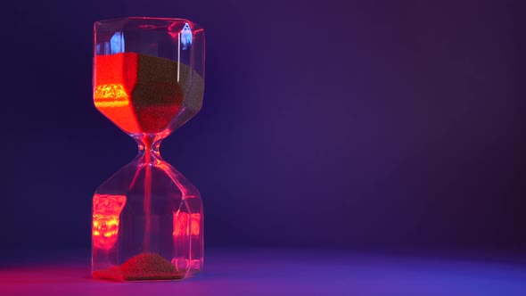 Glass Hourglass with Golden Sand on Purple Background alt