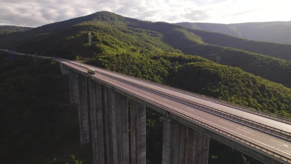 Top View of Single Cargo Semitruck Driving on Highway Viaduct with Green Hills in the Back alt