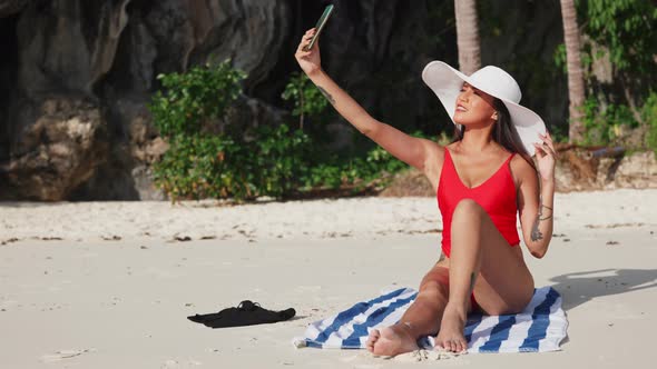 Woman Sitting On Beach Taking Selfie With Smartphone alt