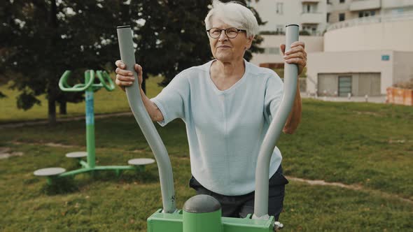 Gray Haired Granny Exercising at Outdoors Gym Playground Equipment alt