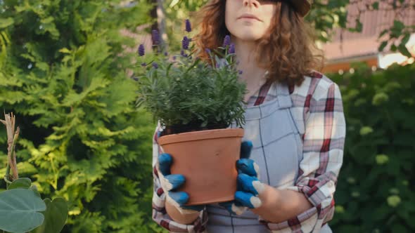 Young Female Gardener Sniffs Lavender Plant in Pot Outdoors alt