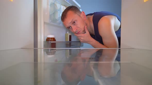 man looks into an empty refrigerator and takes out bottle of alcohol. Alcoholism alt