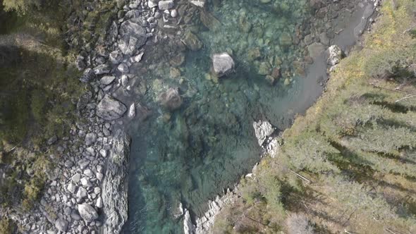 Aerial top view of a blue cold river flowing through summer green forest and stones alt