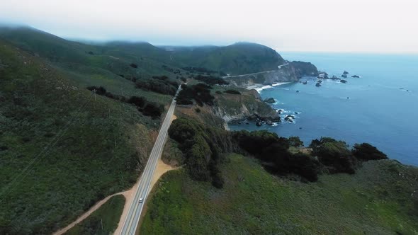 Drone footage of coastal road and misty green hills near the Kasler Point, California, USA alt