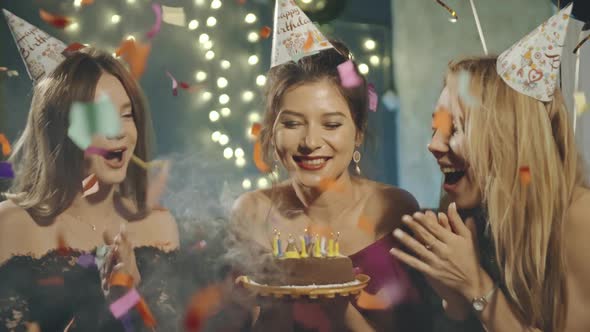 Portrait of Attractive Asian Girl Blowing Out Fire Candles on Birthday Cake Under Falling Glowing alt