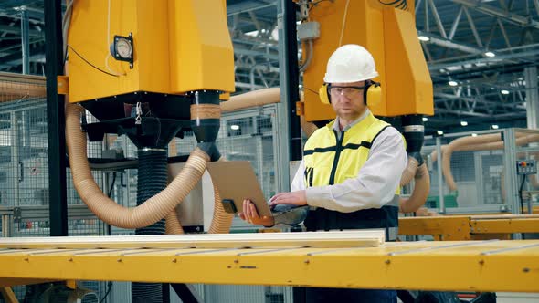 Factory Worker with a Laptop is Observing a Moving Fiberglass Item alt