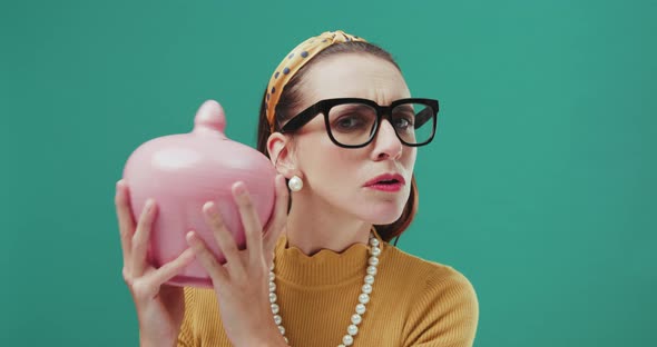 Funny sixties style woman shaking a money box checking her savings, looking sad. Isolated.