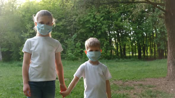 A boy and a girl in medical masks stand in a Park against the background of the setting sun .