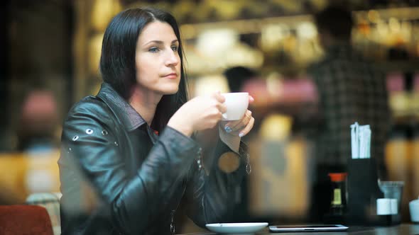 Beautiful Young Woman Dreaming with Cup of Hot Coffee Over Window in Cafe alt