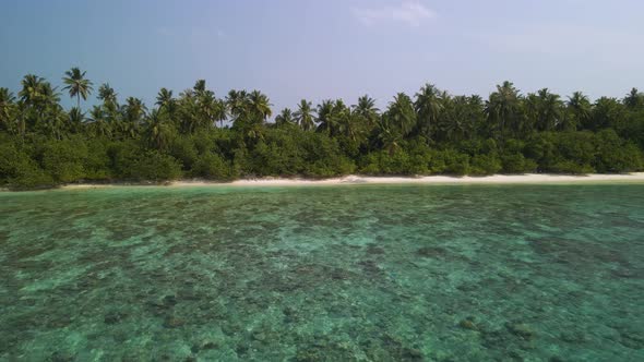 Drone flying from an island with green trees towards the open ocean with blue water and rocks in it alt