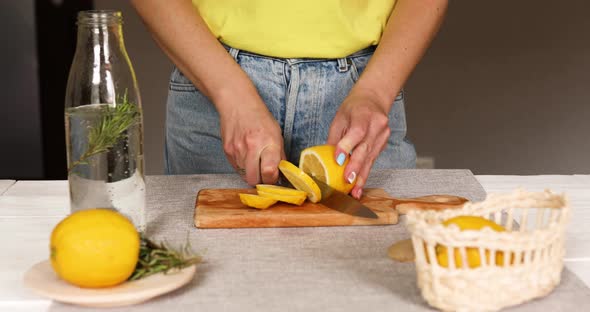 Female hand cut lemon making detox healthy water with lemon and rosemary alt