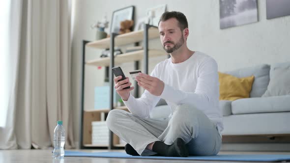 Man Making Online Payment on Smartphone on Yoga Mat alt