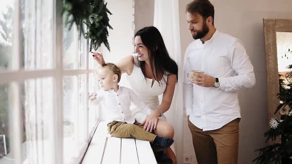 Young Lovely Family Sitting Together By the Window Decorated with Christmas Wreath alt