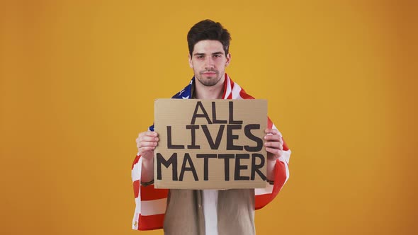 Young Guy Wrapped in Flag of USA is Raising Up Cardboard Tablet with Inscription All Lives Matter alt