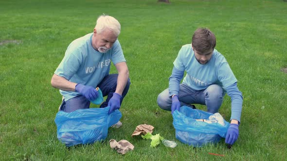 Young and Mature Men Collecting Trash in Garbage Bag Giving High Five, Teamwork alt