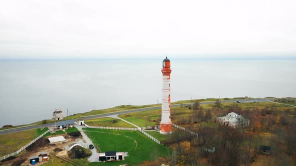 Drone Flying Above Scenic Old Lighthouse and Picturesque Farm Buildings on Overcast Baltic Sea Shore alt