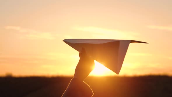 Woman Launches Paper Airplane Against Sunset Background alt