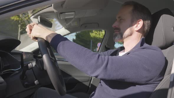 A Middleaged Handsome Caucasian Man Waves at the Camera with a Smile in His Car  Closeup