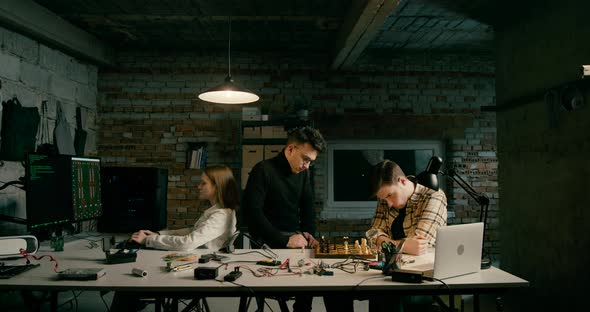 Men Play Chess Working in Electronics Technology Startup in Loft Office at Night