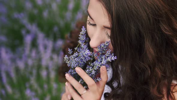 Closeup Portrait of a White Girl Sniffing Lavender Flowers in a Summer Bright Dress Lavand Field
