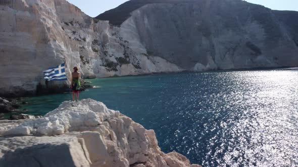 Greek woman with flag on Plakaki beach cliff. Aerial view alt