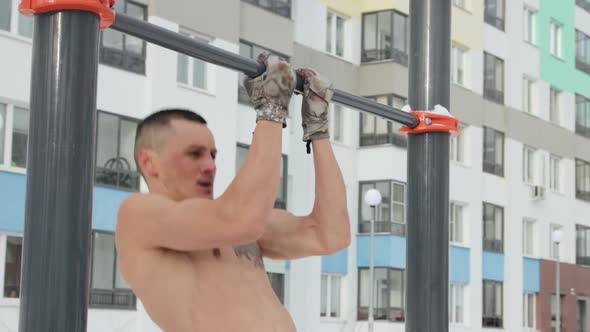 Muscular man training topless on sports field in winter