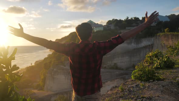 Young Man Traveler Raising His Hands High on Top of the Mountain Above Beautiful Landscape on Golden