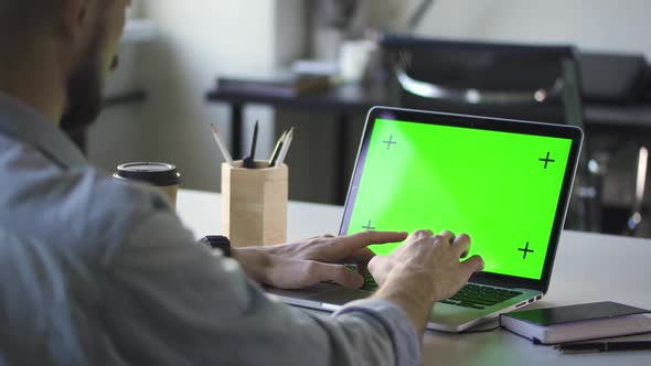 Young Businessman Typing on Laptop and Drinking Coffee at Table in White Office alt