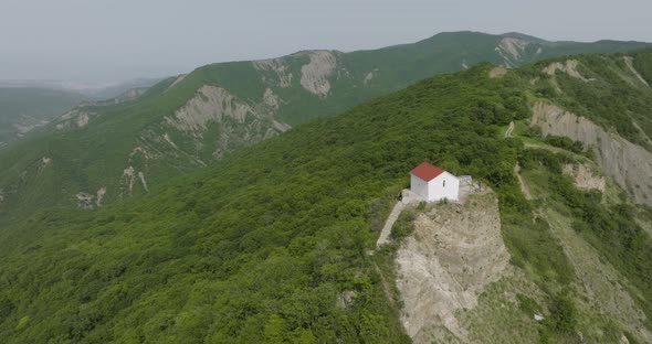 High angle aerial shot of a small building surrounded with forested hills. alt