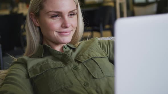 Caucasian businesswoman sitting on pouf using a laptop in modern office alt
