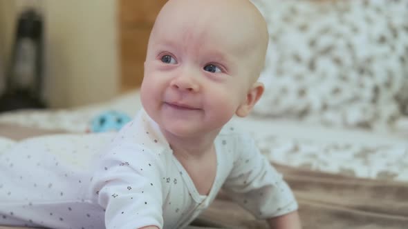 happy baby lies on his stomach on the bed leaning on his hands